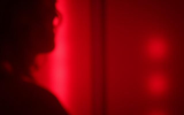 Close-up of a red light therapy panel emitting a deep red glow with a soft human silhouette in the background